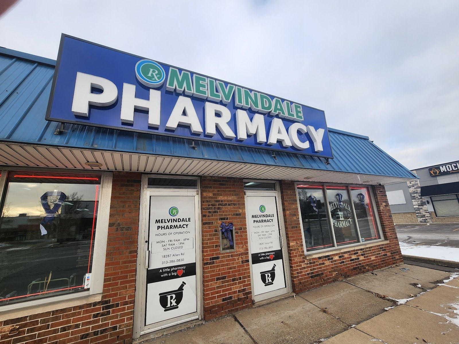 The Melvindale Pharmacy storefront on Allen Road: a brick front under a blue metal roof with a large blue MELVINDALE PHARMACY sign